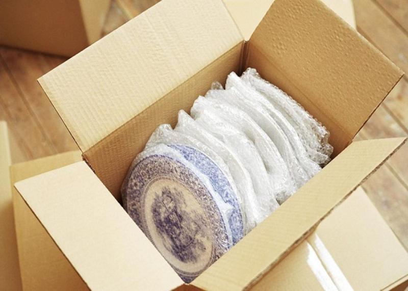 Hình ảnh một người đang đo kích thước của một thùng carton hình hộp chữ nhật để chuẩn bị đóng gói hoặc vận chuyển, minh họa ứng dụng thực tế của việc tính thể tích