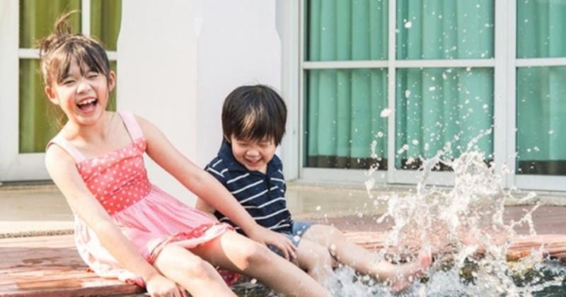 Minh họa một học sinh lớp 4 đang ngồi trên ghế sofa đọc một cuốn sách tiếng Việt. Bé cười tươi, thể hiện sự thích thú. Xung quanh có nhiều sách khác và một vài đồ chơi giáo dục rải rác.